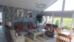 A modern living room with a grey sofa set, a coffee table, and a dining table with chairs. There are two wall-mounted artworks depicting animals.