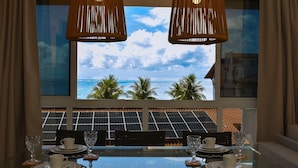 A dining area with a table set for four, overlooking a scenic ocean view with palm trees and solar panels below. - Mila Rooftop (Tamandaré)