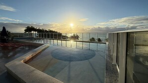 A rooftop infinity pool with a view of the sunset over the ocean, a glass railing, and a lounge area with chairs. - Mila Rooftop (Tamandaré)