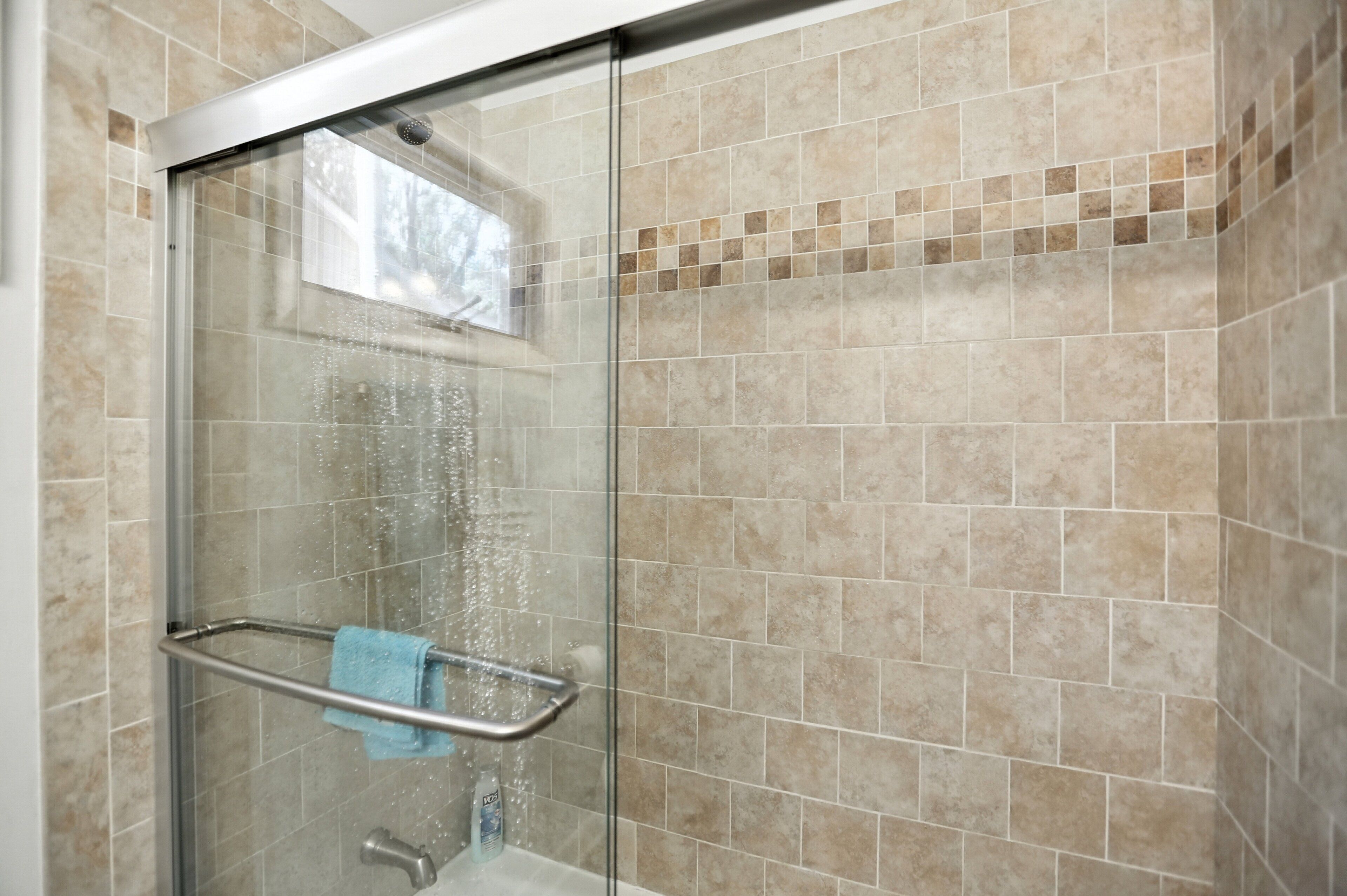 Une douche fermée par des parois en verre, dotée d’une barre d’appui en métal et d’un porte-serviettes.