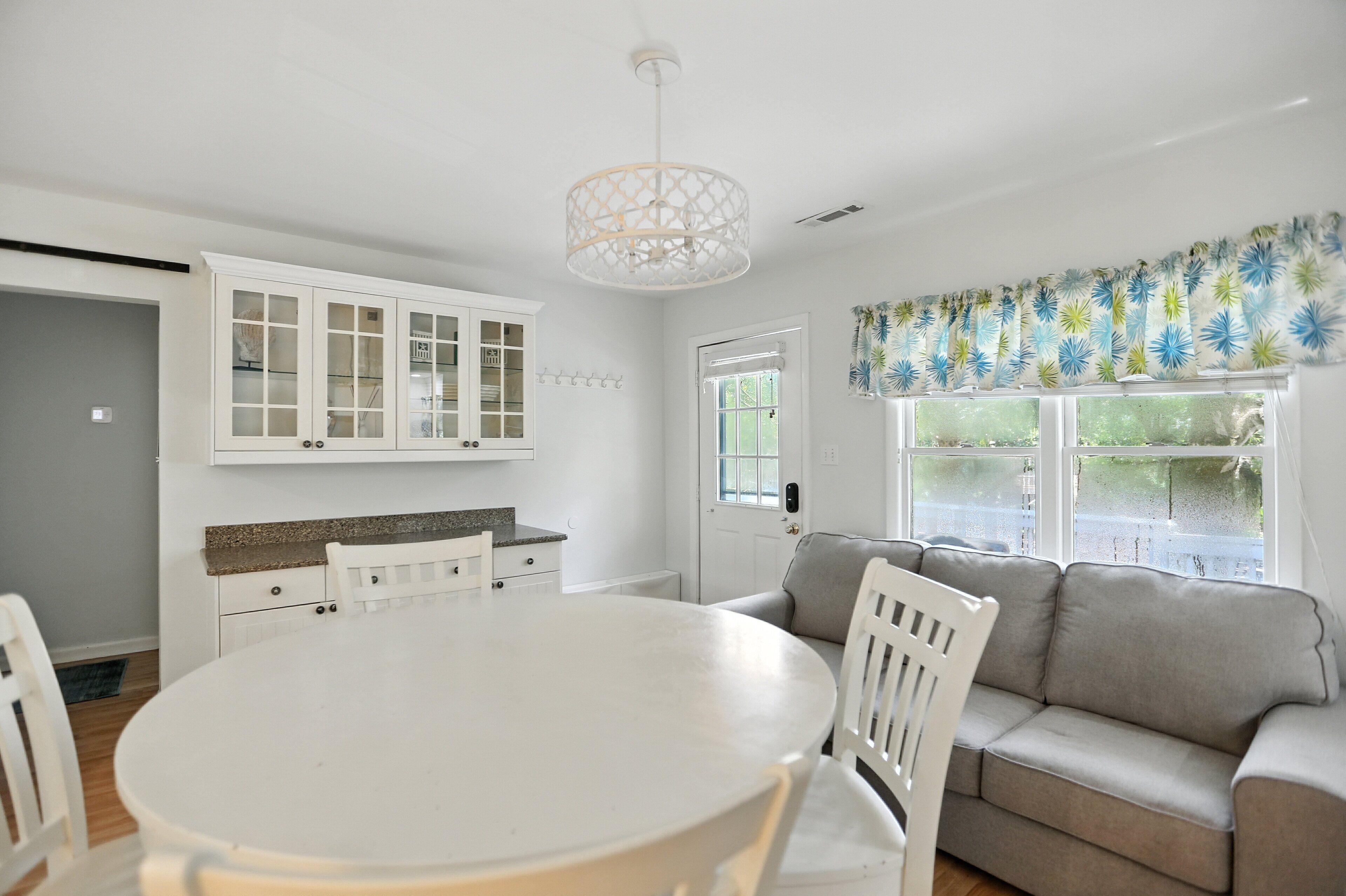 A modern kitchen with white cabinetry, a round dining table, and a grey sofa.