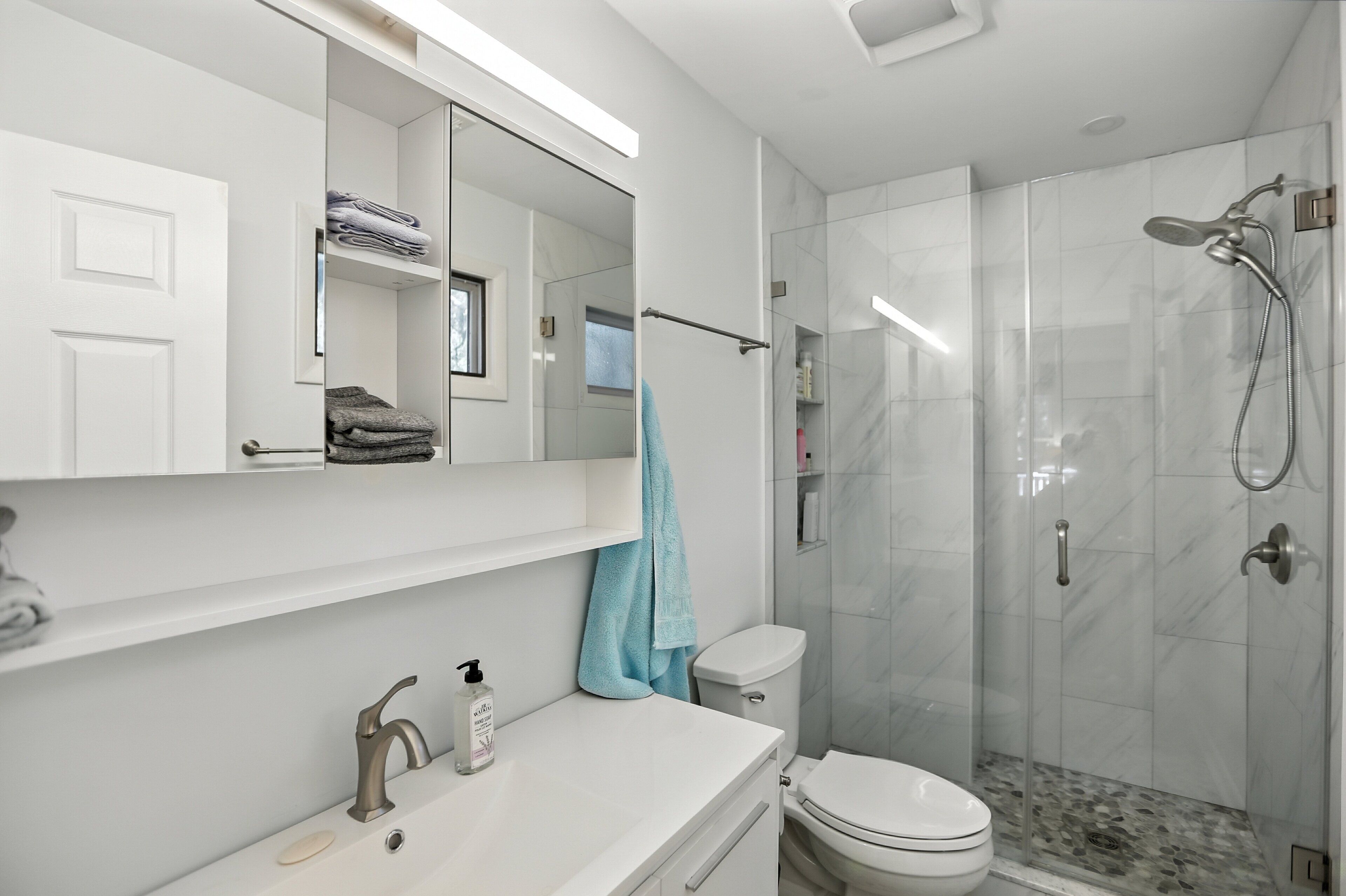 Un baño moderno con tocador blanco, cabina de ducha de vidrio y un inodoro.