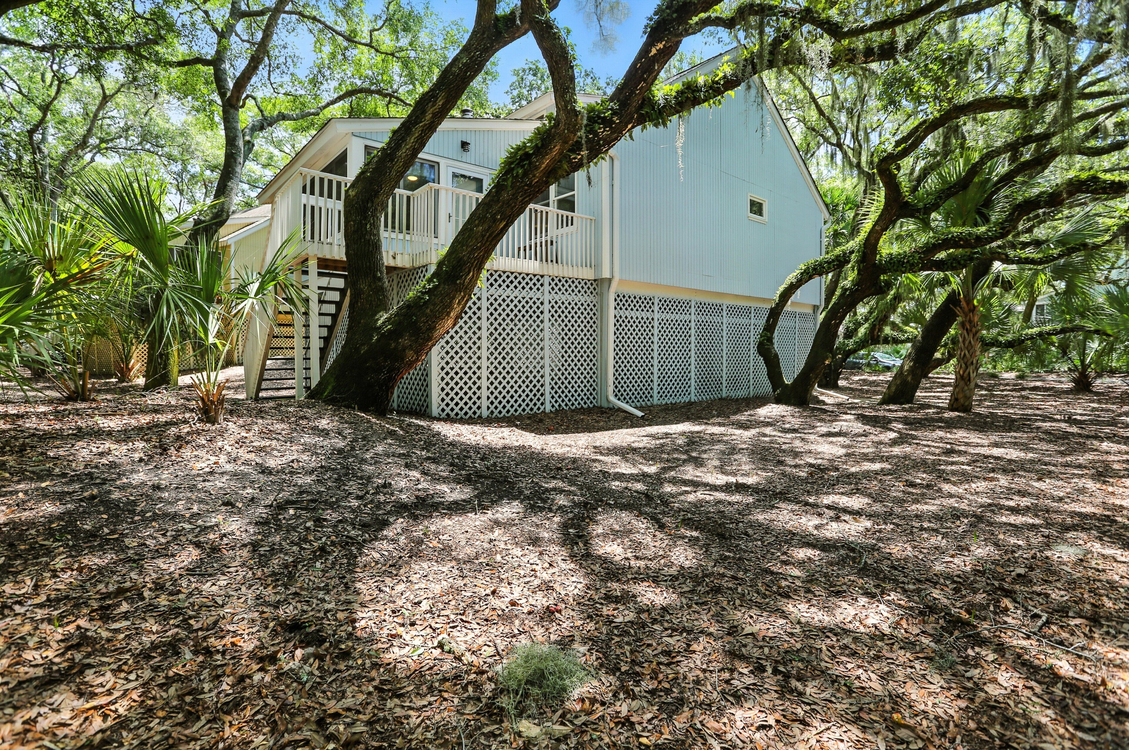 A light blue building with a white balcony, surrounded by trees and a wooden fence.