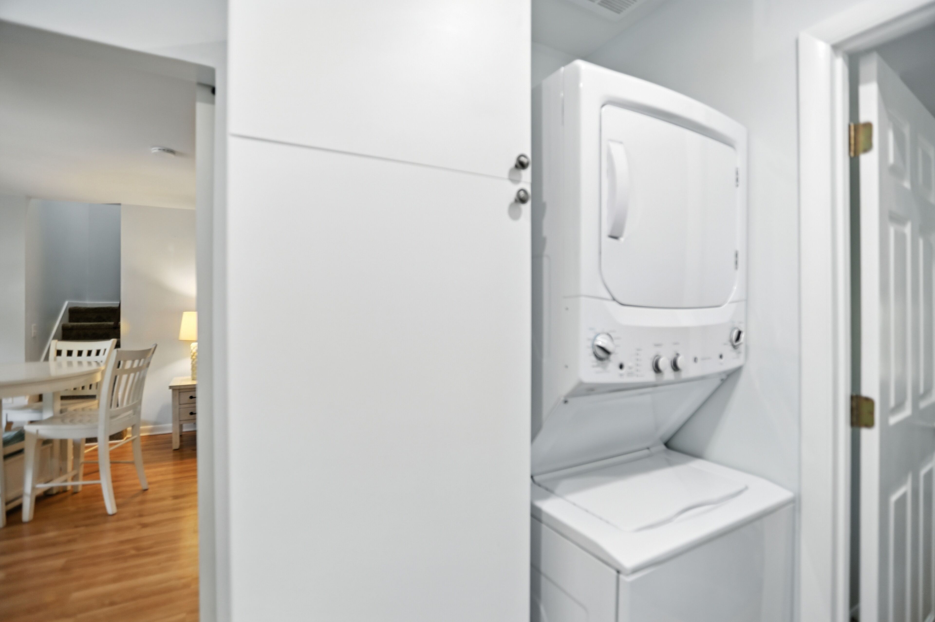A compact laundry room with a white washing machine and dryer, a small table with a chair, and a desk with a lamp.