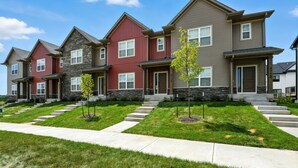A row of modern townhouses with a central driveway, stone accents, and small trees. - Modern Townhome Retreat In Prime Location 3 Bedroom Townhouse (Iowa City)