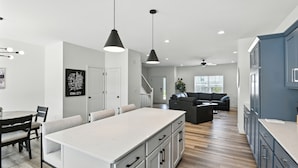 A modern kitchen with a large island, pendant lighting, and a dining area with chairs and a table. - Modern Townhome Retreat In Prime Location 3 Bedroom Townhouse (Iowa City)