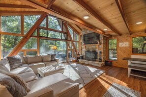 A spacious living room with a large sectional sofa, a fireplace, and large windows offering a view of the surrounding forest. - Aspen Ridge by Innsbrook Vacations! (Innsbrook)
