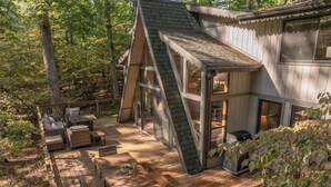 Une cabane moderne dotée d’une terrasse en bois, d’un espace salon extérieur et d’une grande fenêtre donnant sur la forêt.