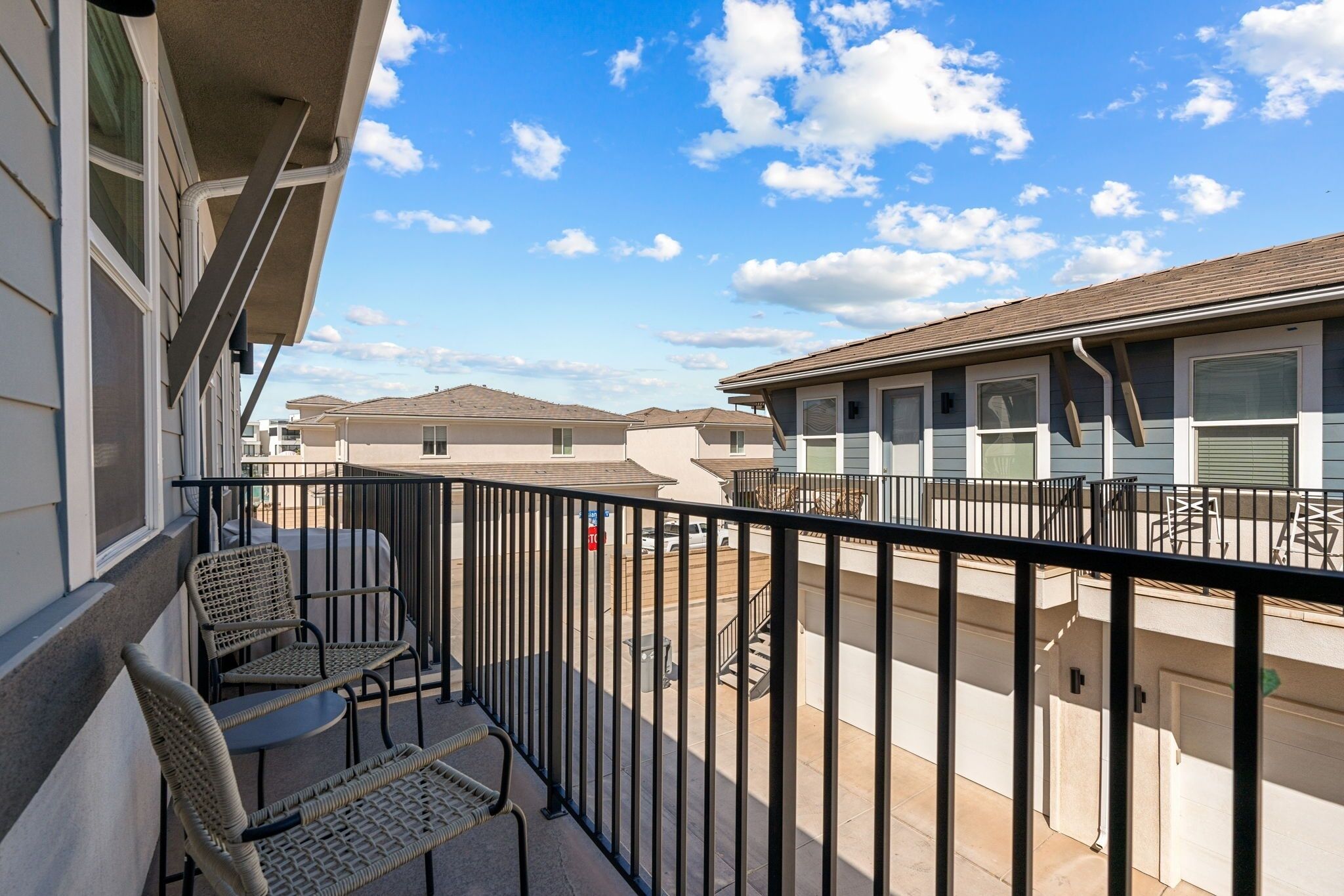 A balcony with wicker furniture, a view of neighboring buildings, and a clear sky.