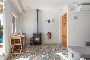 A room with a tiled floor, a wooden table with chairs, a black stove, a fire extinguisher, and a door with a wooden frame.