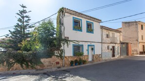 A street view with a two-story building featuring a stone facade, blue window frames, and potted plants on the windowsills. - Apartment 'La Manchega' with Mountain Views, Wi-Fi and Air Conditioning (Villar del Arzobispo)