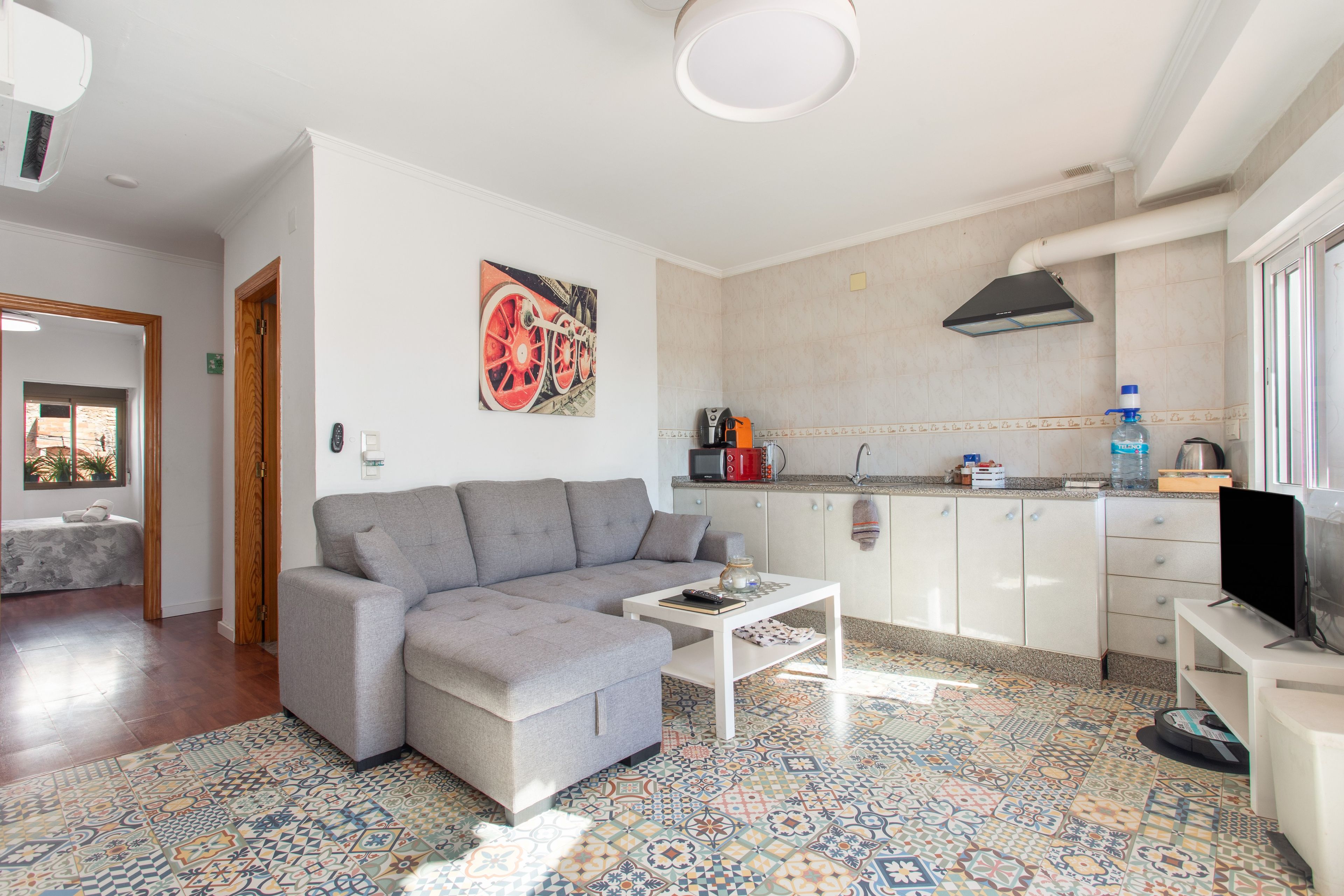 Ein modernes Wohnzimmer mit einem grauen Sofa, einem Couchtisch und einem farbenfrohen, gemusterten Boden.