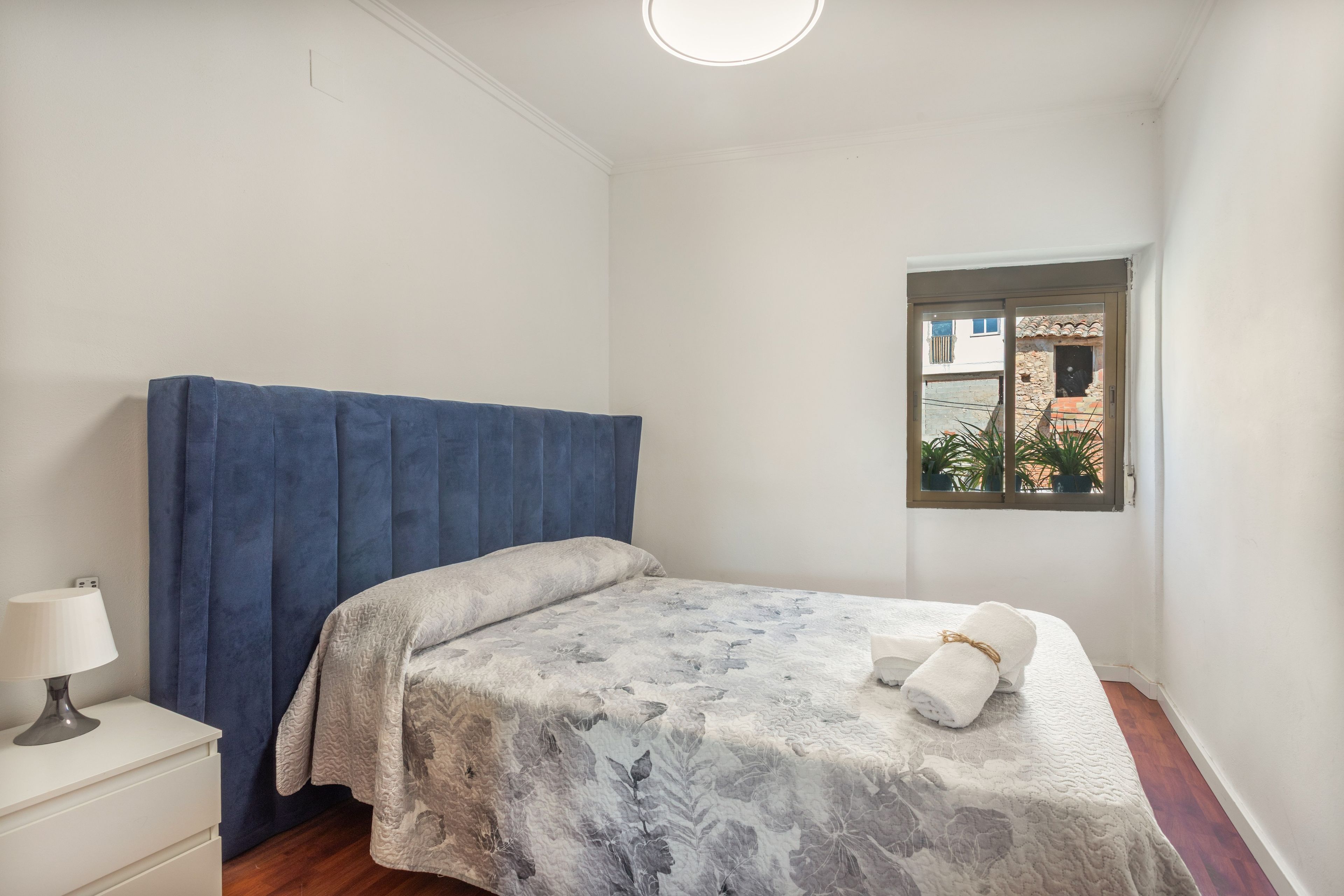 Ein Schlafzimmer mit einem Bett, einem Nachttisch, einem Fenster und Blick ins Freie.