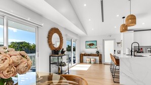 A modern kitchen with white cabinets, a marble island, and a large window offering a view of palm trees.