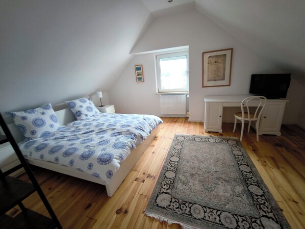 A bedroom with a bed, a desk, a chair, a window, and a radiator. - House Rosalinde (Klüsserath)