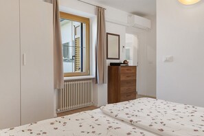 Un dormitorio con cama, cómoda, ventana con cortinas, radiador y espejo.