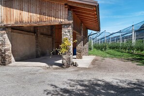 En rustik bygning med stenvægge og en træfacade, en grusvej og et drivhus i baggrunden.