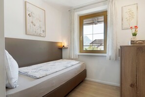 Un lit simple avec une tête de lit, une lampe de chevet, une fenêtre avec des rideaux et une armoire en bois.