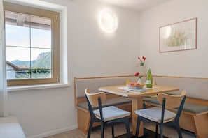 Et spiseområde med et bord, stole og en bænk. Et vindue viser udsigt til bjerge.