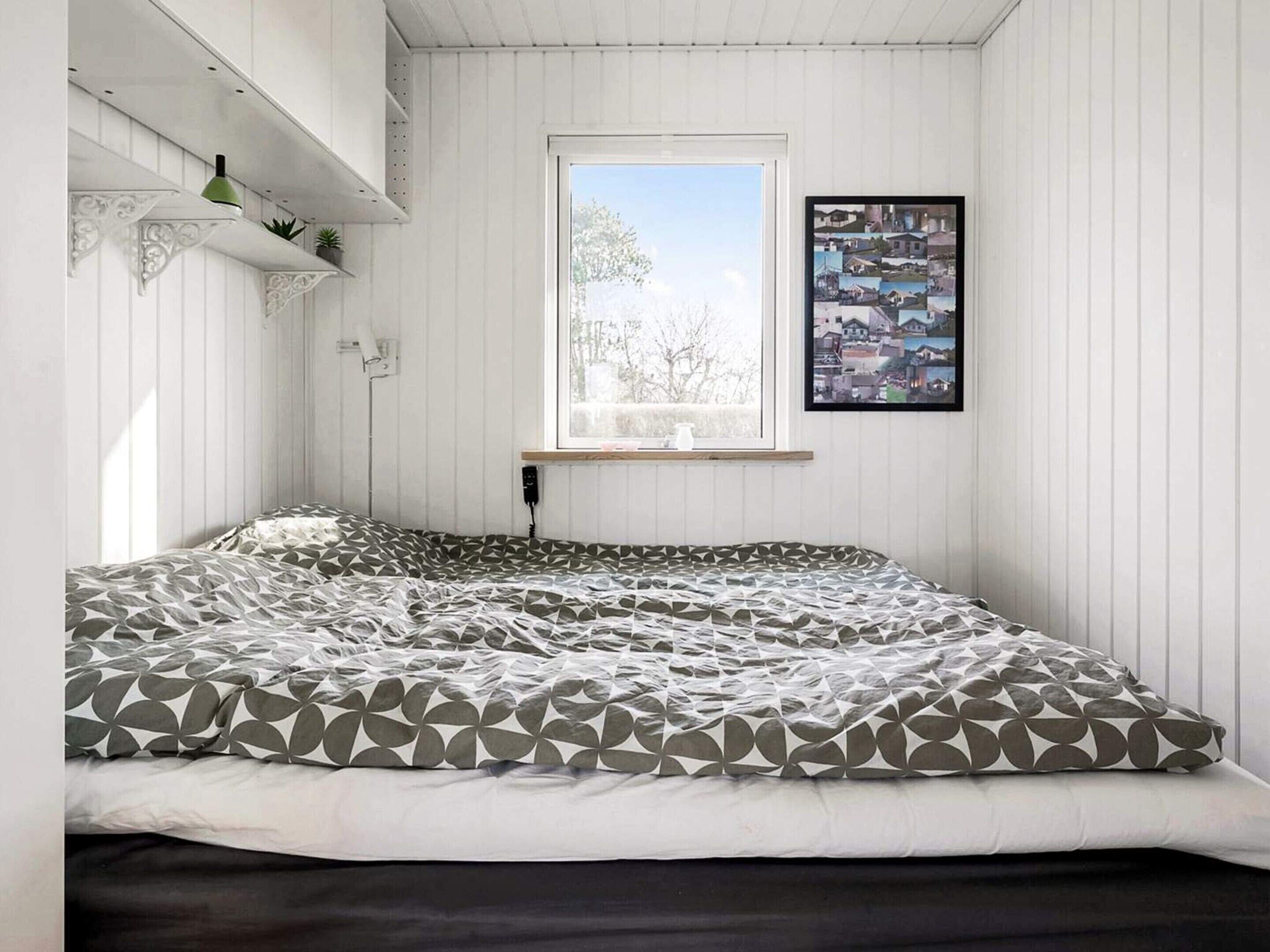 Une chambre à coucher avec un lit, une fenêtre, une étagère fixée au mur et un tableau encadré.