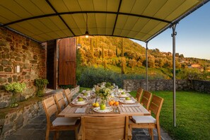 An outdoor dining area with a stone wall, wooden table, and chairs, set against a hillside backdrop. - Villa Giannello Farmhouse (Capannori)