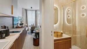 Un moderno baño de hotel con un espejo grande, un lavamanos dorado y una ducha a ras de suelo.