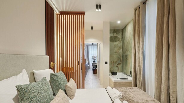 Habitación de hotel con una cama grande, un baño con bañera y vistas al pasillo.