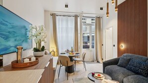 Una habitación de hotel moderna con zona de comedor, sofá y un ventanal con cortinas.