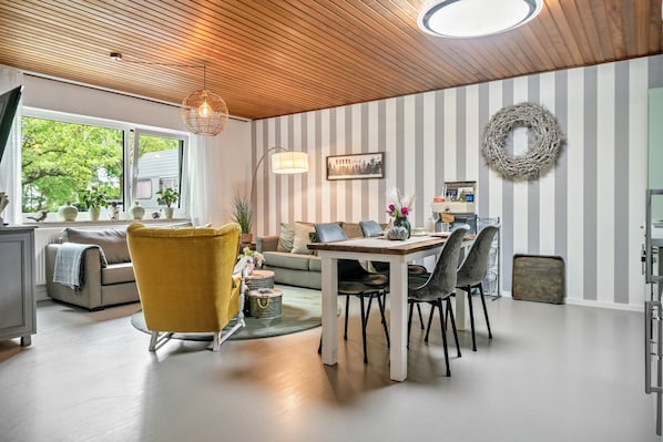 A modern living room with a wooden ceiling, striped walls, a dining table, and a yellow armchair.