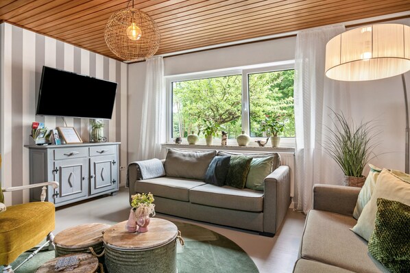 A living room with a sofa, television, and a window with a view of greenery.