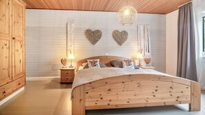 Un dormitorio con cama de madera, dos mesitas de noche, un armario y adornos de pared con forma de corazón.
