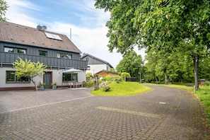 A residential property with a paved driveway, a lawn, and a house with a tiled roof.
