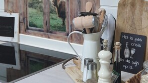 Una cocina con un ventanal rústico, una tabla de cortar, un portavasos para batidores, saleros y pimenteros, y un letrero con una ilustración de una botella de vino.