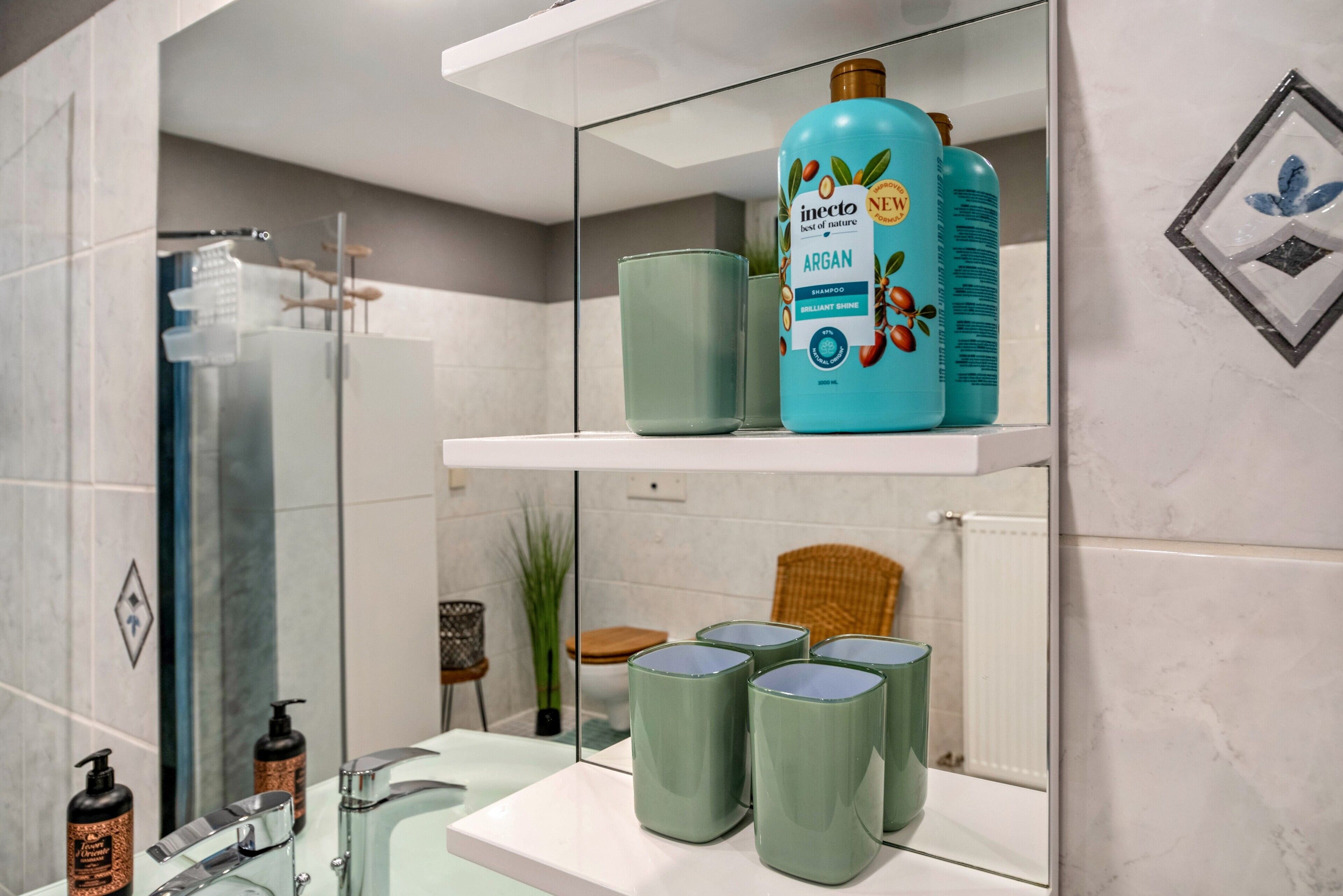 Un baño con cabina de ducha de vidrio, un lavabo con espejo y una repisa con una botella de champú y cuatro recipientes verdes.