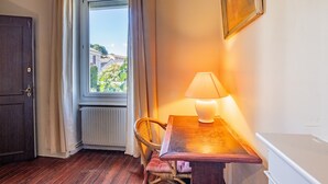A room with a wooden floor, a table with a lamp, a chair, a window with curtains, and a radiator. - Bed and Breakfast 'Chambre Spacieuse' with Shared Terrace, Shared Garden and Wi-Fi (Le Teil)