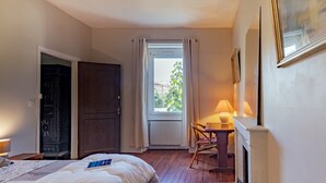 A hotel room with a bed, a desk with a lamp, a fireplace, and a view through a window with curtains. - Bed and Breakfast 'Chambre Spacieuse' with Shared Terrace, Shared Garden and Wi-Fi (Le Teil)