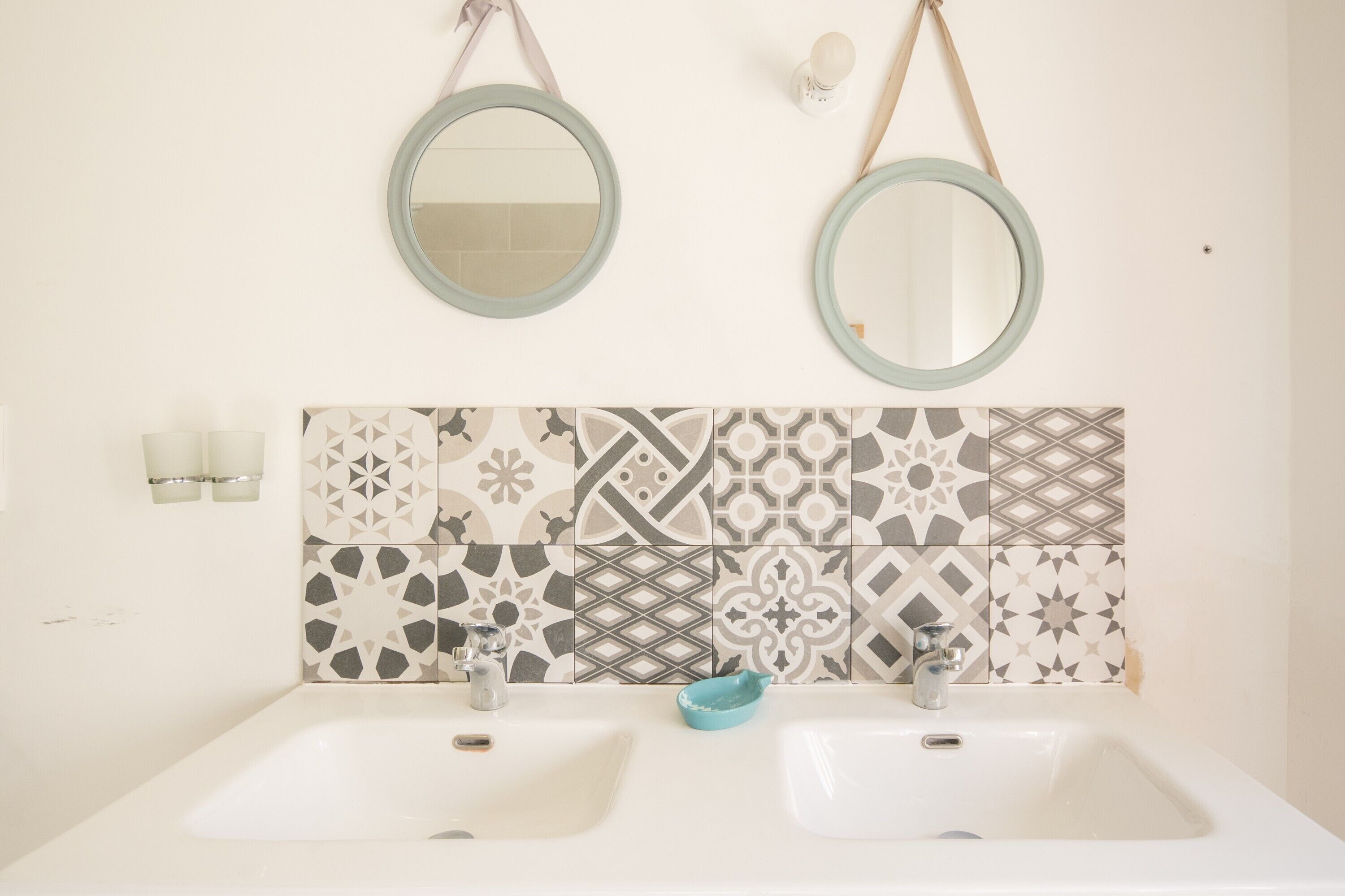 A bathroom with two sinks, a patterned tile backsplash, and two wall-mounted mirrors.