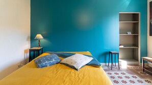 A room with a bed, a nightstand, a lamp, a bookshelf, and a patterned rug. - Apartment 'Bleue' with Shared Terrace, Shared Garden and Wi-Fi (Le Teil)