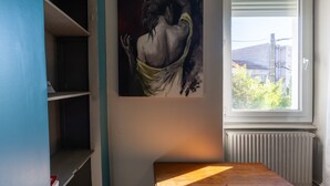 A room with a window, a radiator, a wooden table, and a painting on the wall. - Apartment 'Bleue' with Shared Terrace, Shared Garden and Wi-Fi (Le Teil)