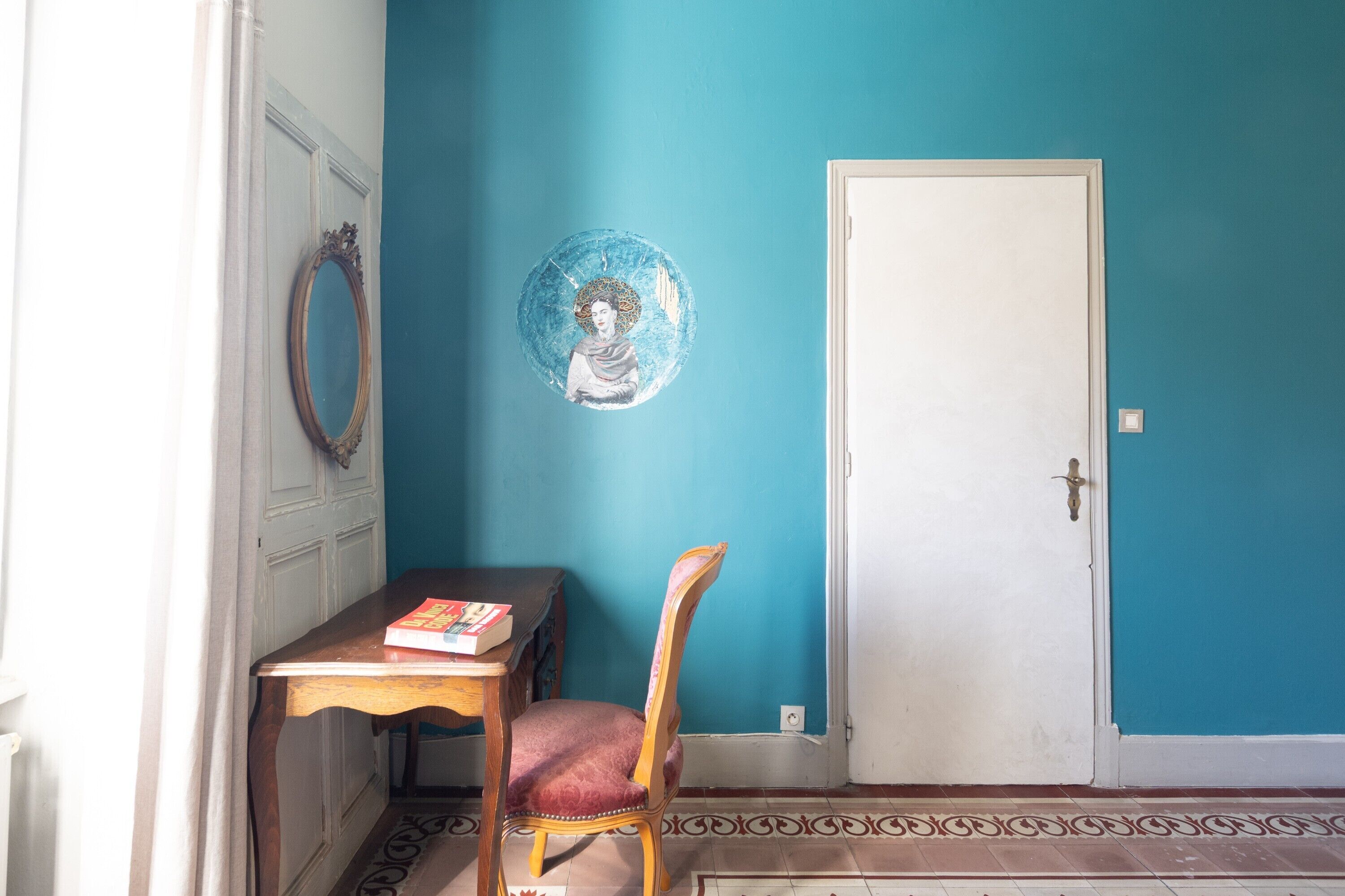 A room with a teal wall, a white door, a wooden table with a book, and a chair.