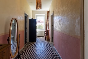 A hallway with a checkered floor, a mirror, and a door leading to a bright room.