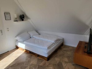 A small, modern bedroom with a single bed, a wooden nightstand, and a TV on a wooden cabinet. - To complete (Oberschleißheim)