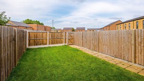 A fenced backyard with a grassy lawn and a brick building in the background. - Luxury 2br in Salford, Slps 6, Wifi, Parking & ps5 (Salford)