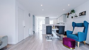 A modern living room with a blue armchair, a purple ottoman, and a dining area with a table and chairs. - Luxury 2br in Salford, Slps 6, Wifi, Parking & ps5 (Salford)