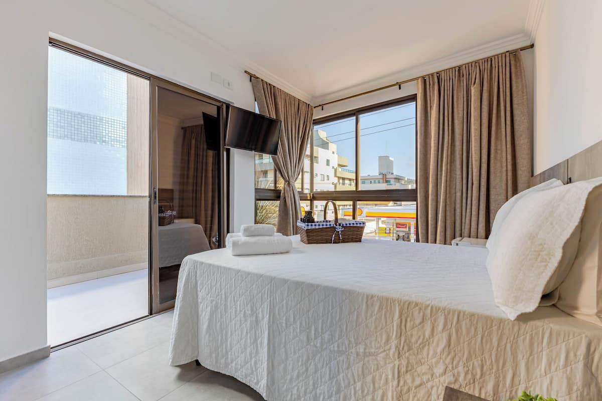 Une chambre d’hôtel dotée d’un grand lit, d’une télévision à écran plat, d’un balcon offrant une vue sur la ville et d’un coin repas avec une table et des chaises.