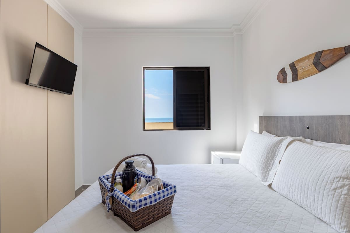 Une chambre à coucher avec un lit, une télévision, une fenêtre donnant sur un paysage agréable et un panier contenant divers objets.