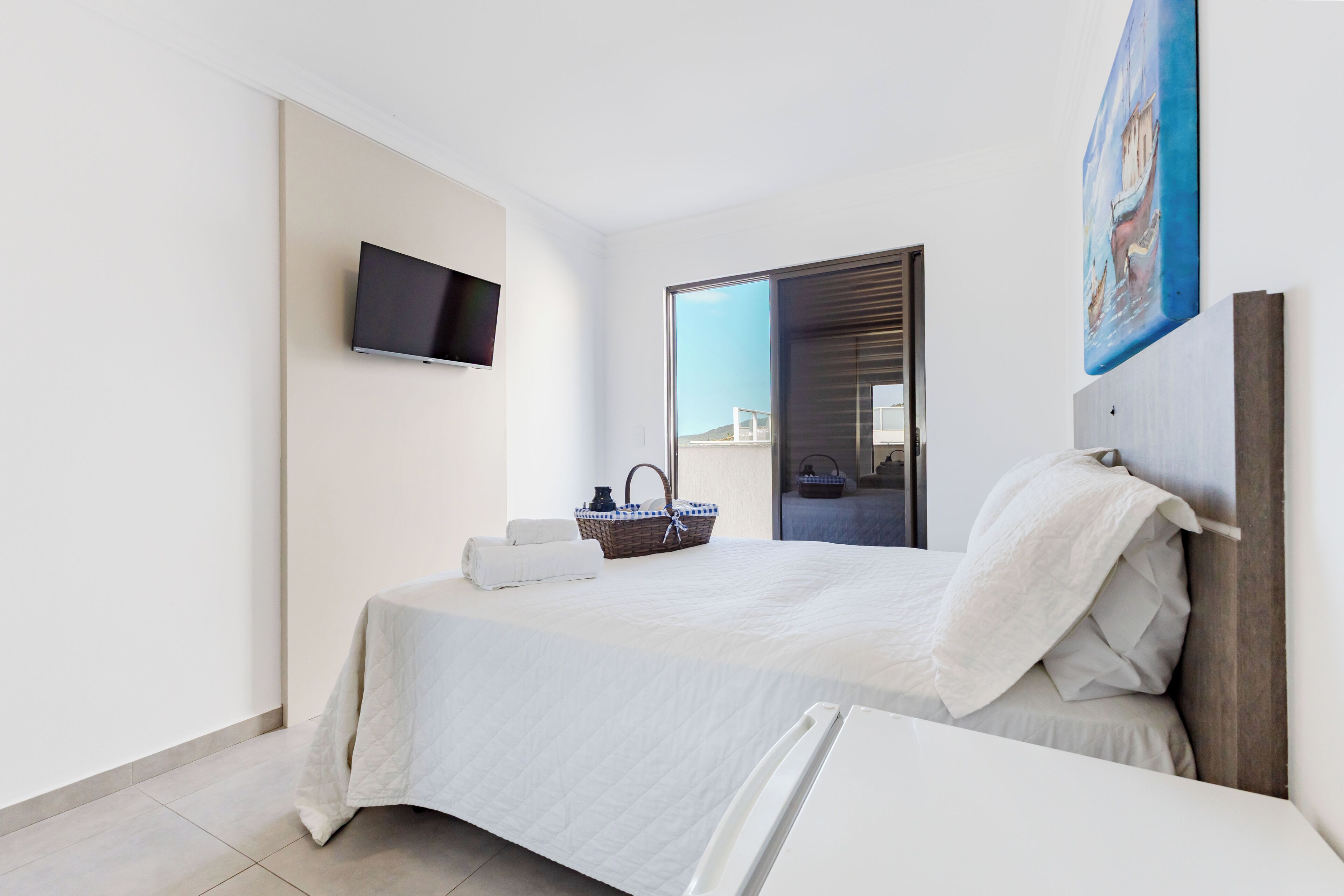 Una habitación de hotel moderna con una cama, un televisor de pantalla plana, una ventana y un cuadro en la pared.