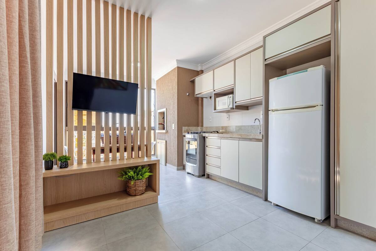 Une cuisine moderne avec un téléviseur à écran plat fixé sur un mur en bois, des appareils en acier inoxydable et des meubles de couleur claire.