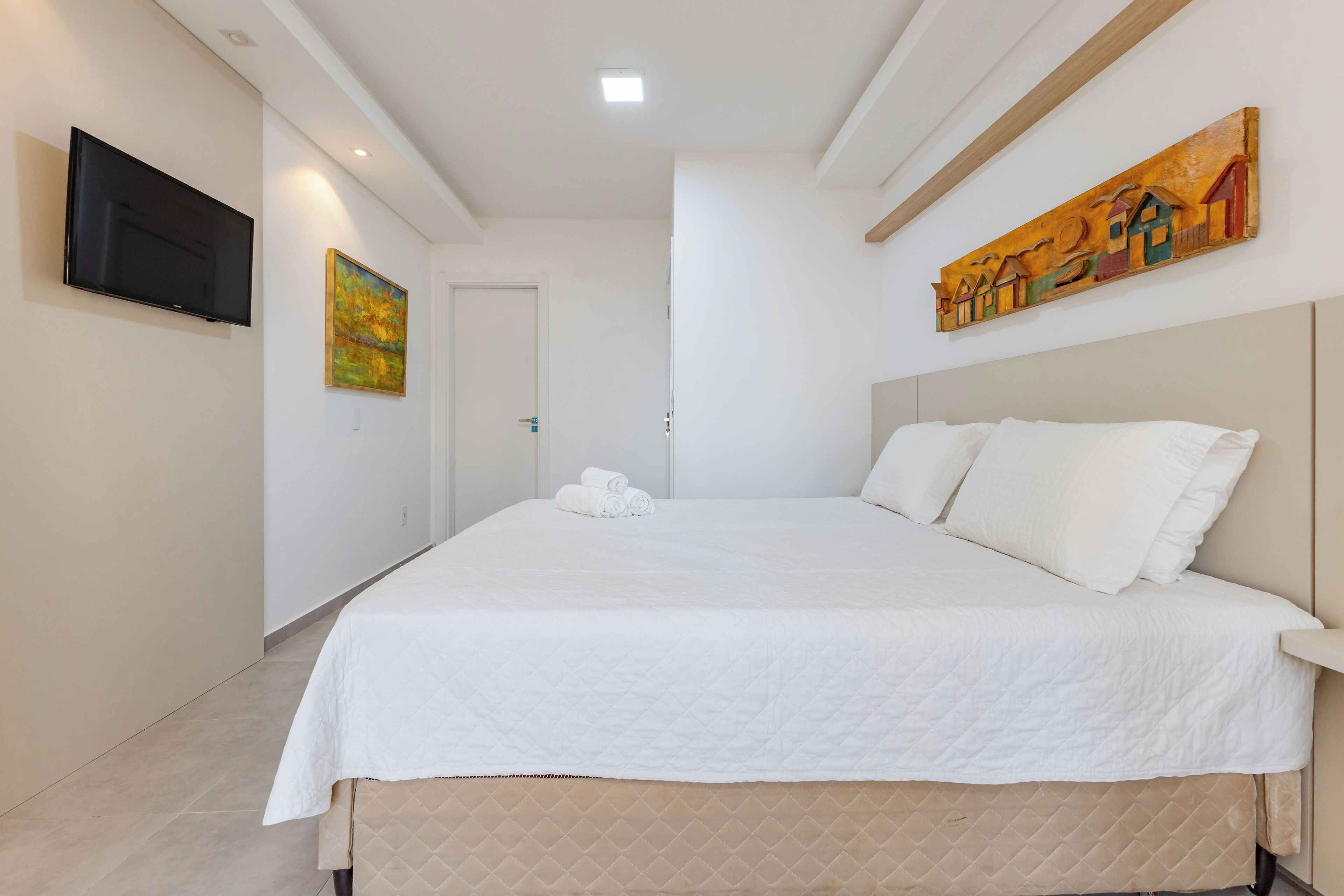 Ein Schlafzimmer mit einem großen Bett, einem flachbildfernseher an der Wand und einem Gemälde über dem Bett.