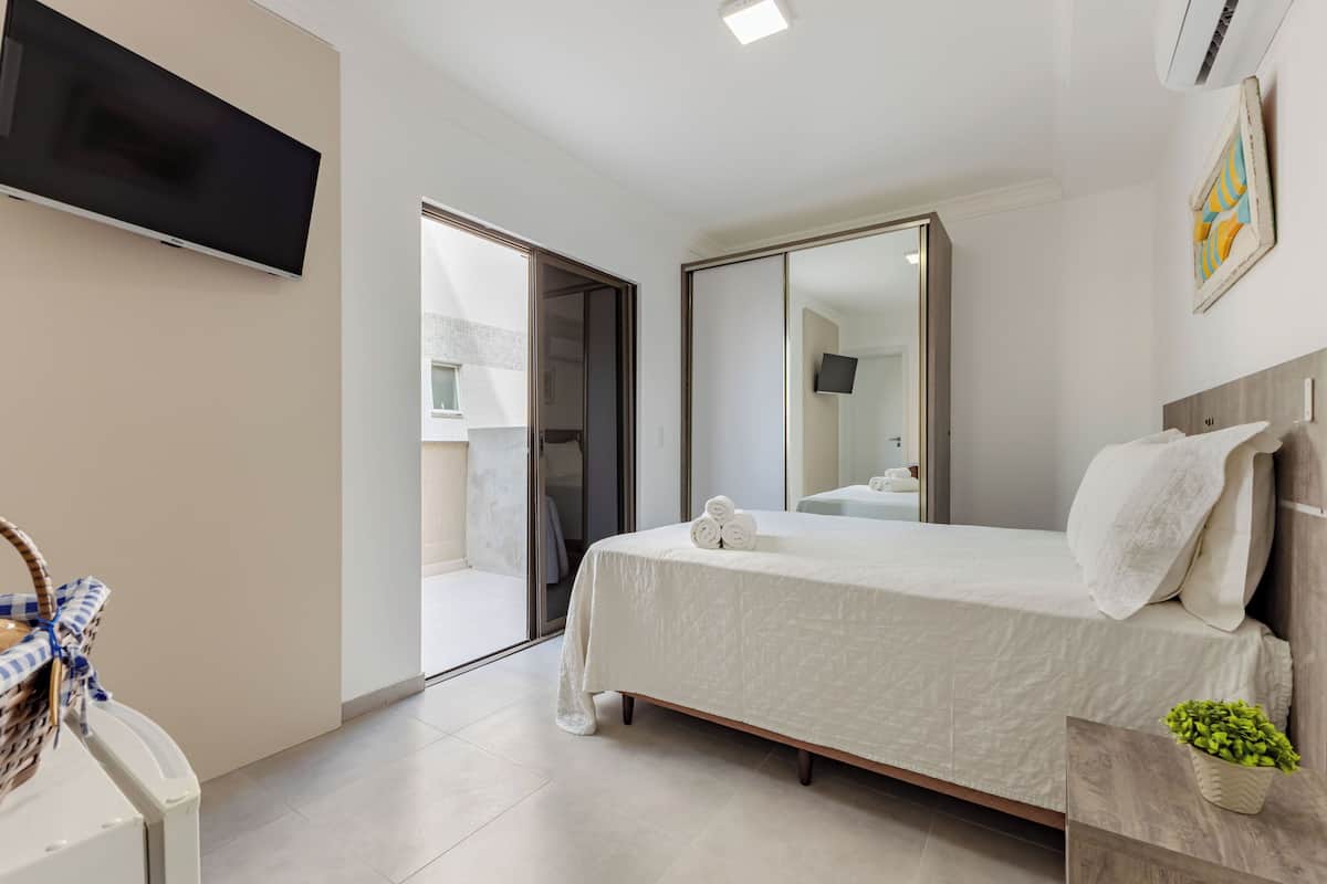 Une chambre à coucher moderne avec un lit, un téléviseur à écran plat, un grand miroir et une petite plante.